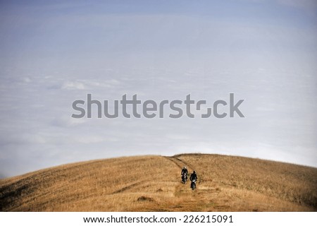 Two motorcycles riding on a mountain plateau above the clouds
