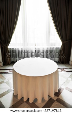 Sunlight falls on an empty round dinner table in a festive marble room