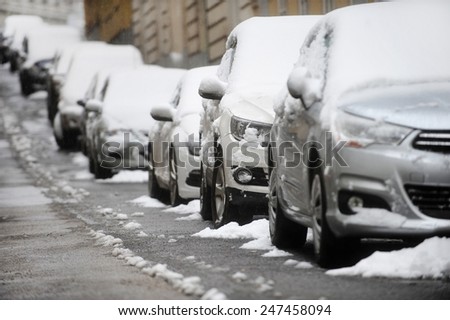 Urban scene with parked cars in a row covered with snow during a snowfall
