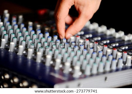 Man\'s hand on a professional audio mixing console with adjusting knobs