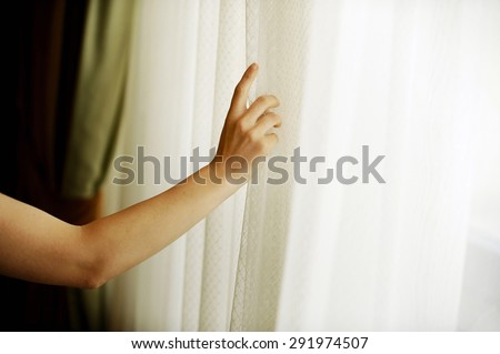 Hand pulling a window curtain for warm daylight to enter the room