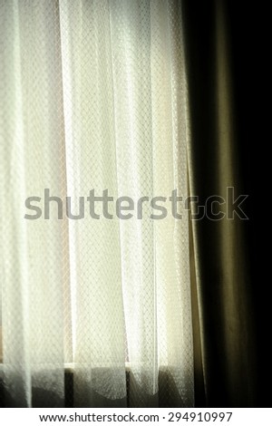 Interior detail with a green velvet window curtain shot against warm outdoor light