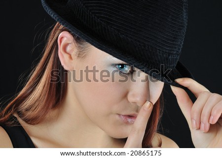 girl hold finger near nose and other hand hold on the hat