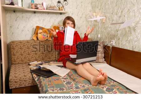 Beautiful young student with flying papers and laptop on sofa