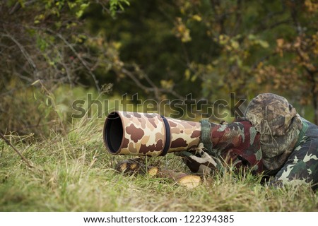 wild life photographer with long telephoto lens in action dress of camouflage