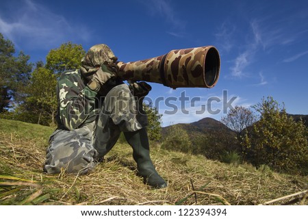 wild life photographer with long telephoto lens in action dress of camouflage
