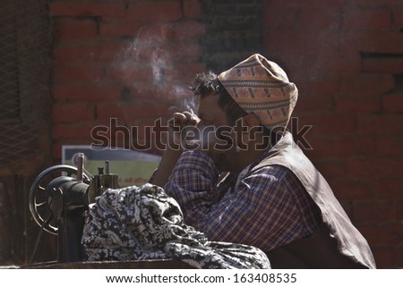 Kathmandu, Nepal - October 23, 2013: Unidentified tailor man smoking cigarette on October 23, 2013i n Kathmandu, Dubar square, Nepal, This nepali man is working in outdoor in market.