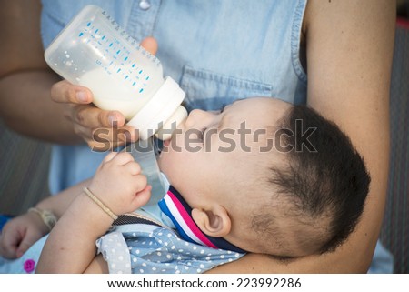Young mother feeding her baby girl with milk bottle on bedroom