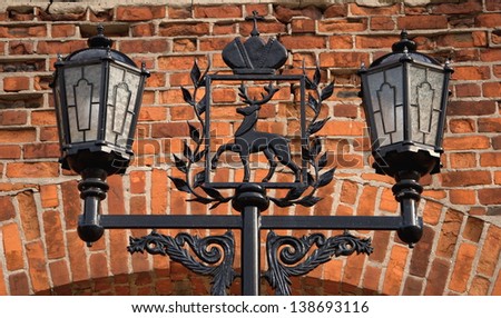 Wrought-iron street lamp, decorated with the coat of arms of the city of Nizhny Novgorod on the background wall of red brick