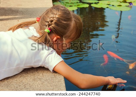 Little girl with pigtails playing with fish in pond