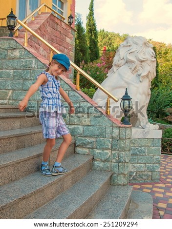 Little girl in cap standing on the stairs of a beautiful house