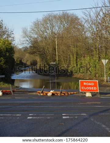 HAMPRESTON, DORSET, UK, FEBRUARY 9, 2014. Flooded road with telephone booth and road closed sign, after severe and prolonged storms along the South coast of England.Wind has knocked over barriers.