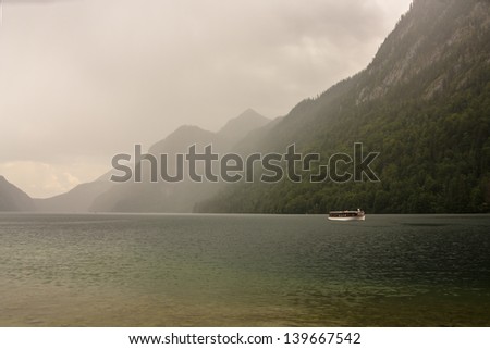 Electric boat on the Kings lake in Germany with Alps in the back, clouds and mist.
