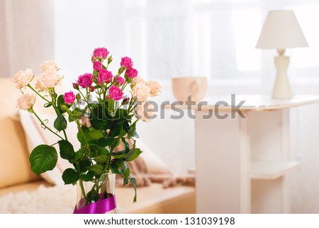 Bouquet of flowers in a room in the interior. Red and white roses in a vase on a table in a bright room. Against the background of the cups and lamps.
