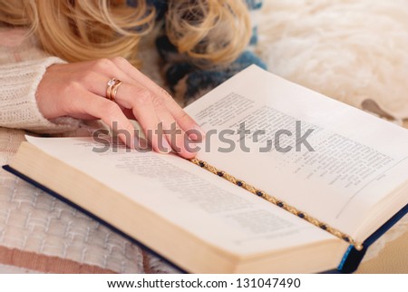 Woman reading a book in the room. Cozy atmosphere. Interesting book. Home to rest. Hand on the page in the book.