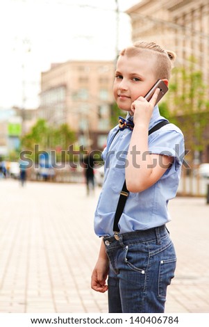 Boy talking on the phone in the city. Beautiful boy with stylish hairstyle in the blue shirt with the phone says in the big city.