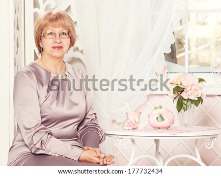 Elderly elegant woman sitting in a lounge. A cup of tea on the table. Older beautiful modern adult woman. Old happy mature woman. Portrait of senior woman. Drinking tea in a beautiful interior. Look.