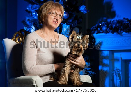 Beautiful modern adult woman. Keep a small dog in her arms. Spending time before trace holidays. Christmas atmosphere in the interior room. Wait until the new year. Portrait of senior woman with dog.
