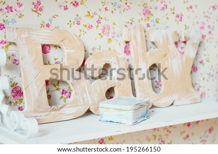 Wooden letter word Baby on a background of vintage wallpaper with small flowers. Inscription, letters, wood, room, shelf - vintage concept.
