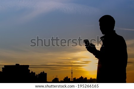 Silhouette of man standing on city background, sunset and blue sky. Man holding a telephone. Silhouette, man, sunset, city, phone - advertising concept of freedom of communication.