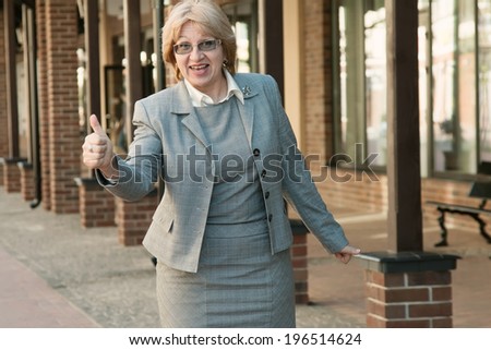 Business woman on modern city background business. Adult woman in a business trip or on a walk. Portrait of a senior business woman showing that things are good. Thumbs up business woman with glasses.