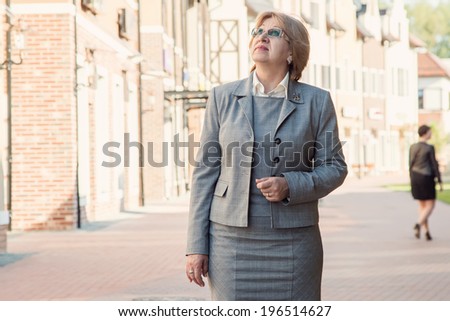 Business woman on modern city background business. Adult woman in a business trip or on a walk. Portrait of a senior business woman showing that things are good. Woman looking on top of something.