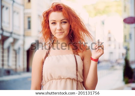 Lucky young modern girl with red hair, walking around the city. Beautiful smile on the face of a happy woman young age. Trips girl on the background of the city with ancient architecture.