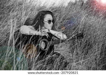 Happy young girl playing guitar outdoors. Woman musician guitarist. Hippie modern movement of the past generation. Music and guitar and fresh air. Sunset summer sun. Black and white photography.