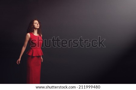 Young beautiful woman in a red dress. A woman comes out of the depression on a dark background. Look, strive toward the goal to achieve relaxation. After a hard state wants to get away.