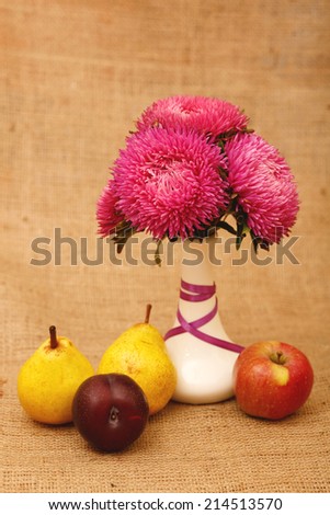 Arrangement of flowers and fruit. Aster flower in white vase on a table stand. Next to them are apple, pear, plum. Autumn still life of fresh fruit and flowers. Composition in yellow tones. Space text