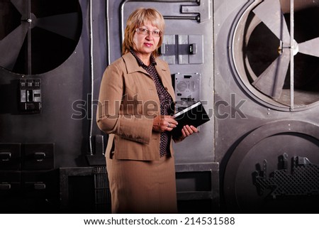 A female engineer. Adult woman working as an engineer at work. Senior Researcher woman holding a book for accounting and statistics of production. Business woman on the background of the turbine.