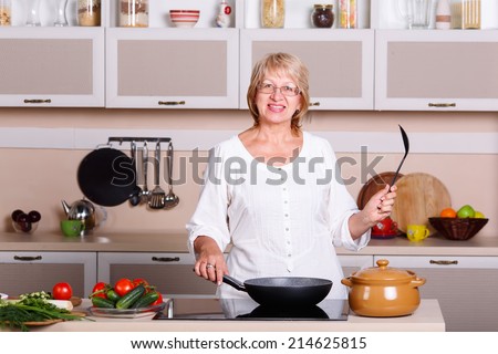 Senior woman cooking in the kitchen. Healthy food. Diet concept. Healthy lifestyle. Cooking at home. Cook meals at home. Woman fries and cooks in kitchen utensils in the kitchen. Pots, pans, stove.