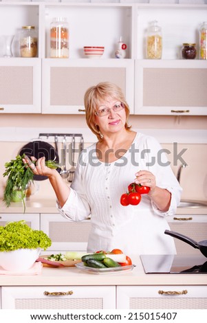 Adult woman working in the kitchen. Mom while she work something else. Mother prepares a salad. Cooking. Woman while preparing food in kitchen. Beautiful adult multiracial woman while making salad.