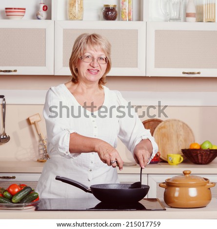 Happy adult multiracial woman while making lunch. Adult woman working in the kitchen. Mom while she work something else. Mother prepares. Cooking concept. Woman while preparing food in kitchen. Retro.