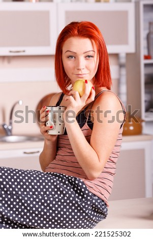 Beautiful young woman drinking tea or coffee in the kitchen. Breakfast kitchen, apple, diet, morning tea - the concept of wellness and a healthy diet of the modern woman. The morning breakfast coffee.
