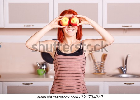 Cheerful good morning in the kitchen. Young woman closes her eyes with apples. Girl holding a red apple. Laughter and joy, smile, diet, healthy, nutrition, fruits, youth, beauty. Concept of lifestyle.