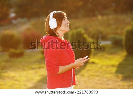 Modern woman with headphones listening to music on her head. Young woman on the nature of urban clothing. Woman lit by the rays of the evening sun at sunset. Good mood, favorite music, happy time. Ok.