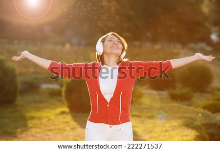 Happiness woman enjoy nature. Beauty girl on the street. The concept of freedom. Beauty girl under the sky and the sun\'s rays. Pleasure. Woman with headphones listening to music on her head.