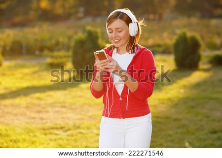 Woman lit by the rays of the evening sun at sunset. Good mood, favorite music, happy time, autumn. Ok. Woman standing listening to music with her mp3 player and headphones against nature
