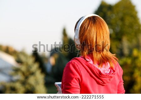 Woman is listening to the music. Stand back. Woman lit by the rays of the evening sun at sunset. Good mood, favorite music, happy time, autumn. Woman with headphones listening to music on her head.
