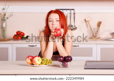Beautiful young woman in the kitchen. Breakfast, kitchen, apple, diet, morning, plum, grape - concept of wellness and a healthy diet of the modern woman. Fresh apples and fruit for morning breakfast.