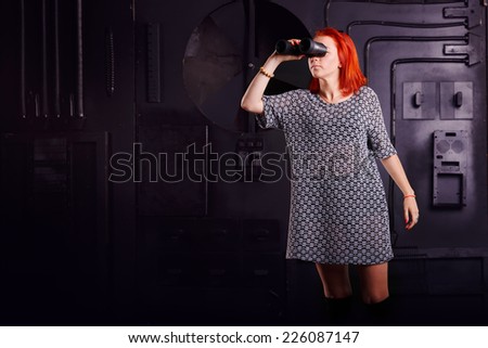 Modern woman looking through binoculars. Girl on a background of technology industrial object with binoculars in hand. Computer games - fantastic hero. Concept title page or enter the game.