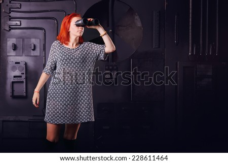 Modern woman looking through binoculars. Girl on a background of technology industrial object with binoculars in hand. Computer games - fantastic hero. Concept title page or enter the game.