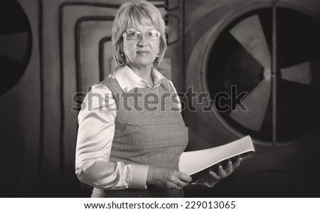 Adult business woman. A woman holding a notebook to take notes. She is against the background of plant production area. She is profession an engineer, technologist, physicist, psychologist. Manager.