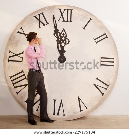 Man standing near the clock. Arrows show the big clock time. Male student or office worker. The clock at five minutes to twelve. Time of onset of the new year. Five minutes to midnight. Make a wish.