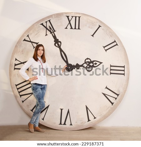Woman standing near the clock. Arrows show the big clock time. Woman student or office worker. The clock at five minutes to three. Time to take a break for lunch and rest. Three o\'clock. Day.