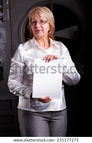 Modern adult business woman holding a white sheet of paper. Woman in business attire holding a table for records. Universal concept for any advertising. Place for an inscription of a woman in her arms