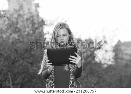 Young modern woman holding an e-book in hand. Girl holding electronic tablet on the background of nature and city. Black and white photo. Modern lifestyle of modern urban woman.