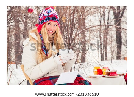 Young woman hid rug and reading book outdoors winter day. Beautiful blonde girl is drinking tea in winter. She is reading a book. Snow, frost, holiday, nature, park. New year. Drink coffee in winter.