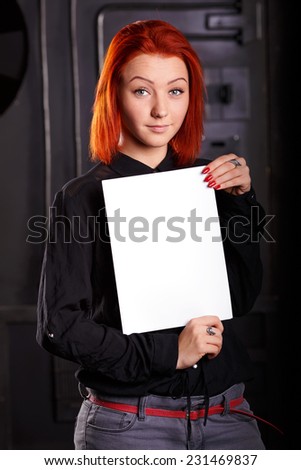 Woman hold blank paper sheet, standing on a dark background. Girl holding a large white sheet as the place for inscriptions. Advertising message that will keep a woman in his hands.